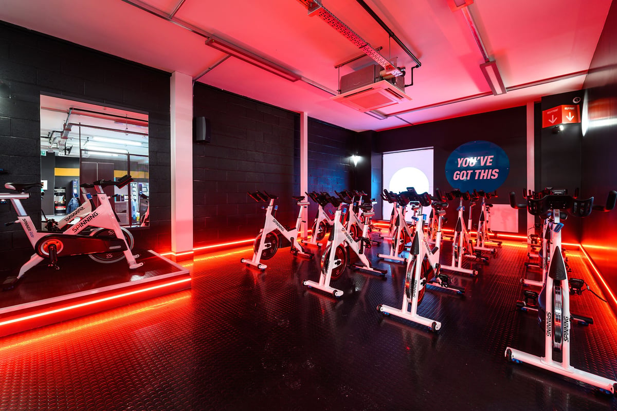 PureGym St Albans: Rows of stationary bikes illuminated by red neon lighting in a sleek fitness studio.