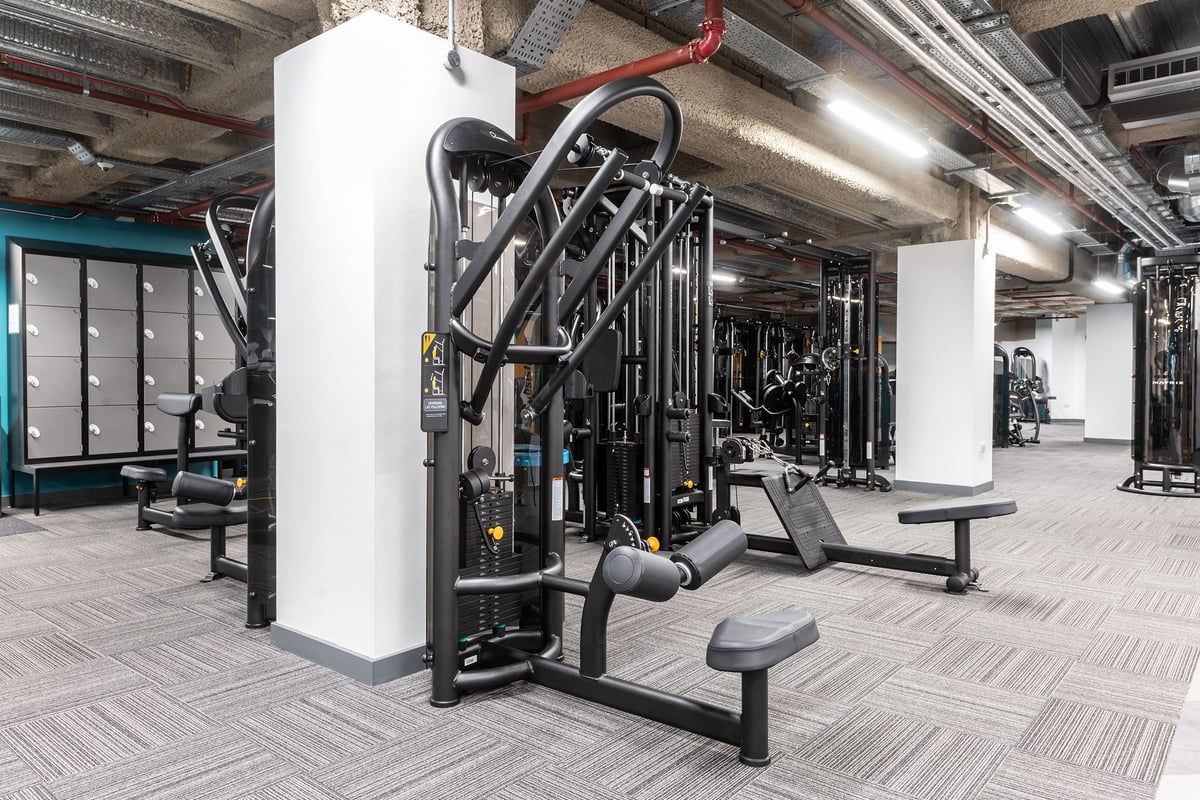 PureGym London Monument: Cable cross machines, weight benches, rubberized flooring in a gym equipment area.