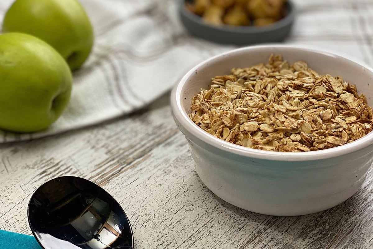 Bowl of oat topping mixture with green apples and nuts on a wooden surface