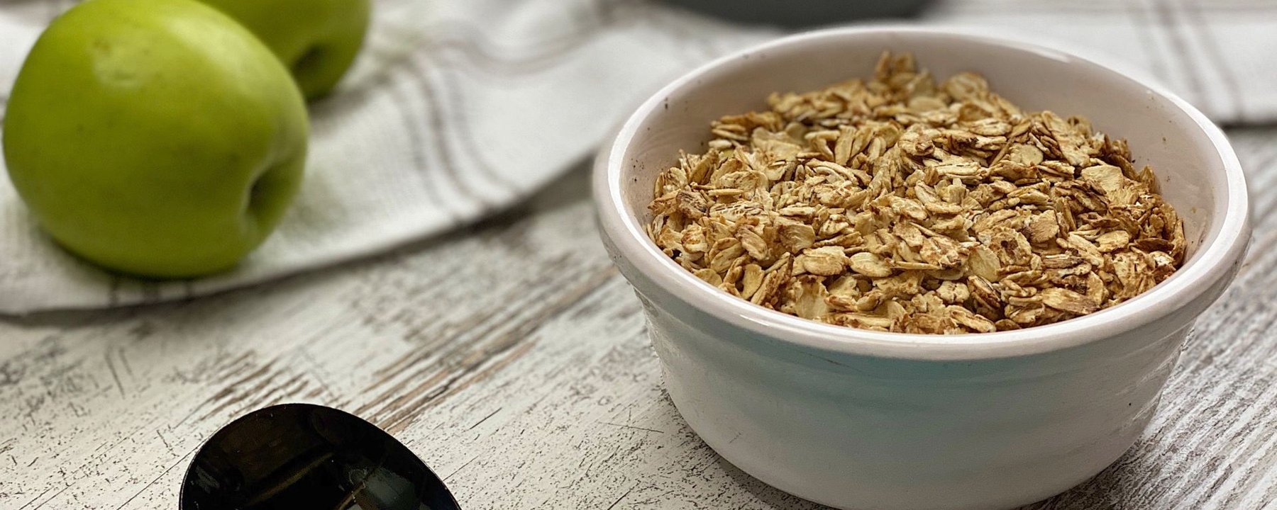 Bowl of oat topping mixture with green apples and nuts on a wooden surface