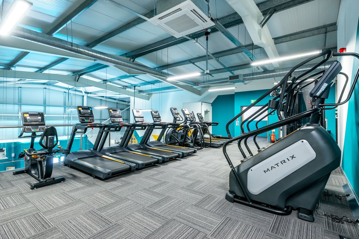 PureGym Market Harborough: Rows of treadmills and an elliptical machine under industrial lighting.