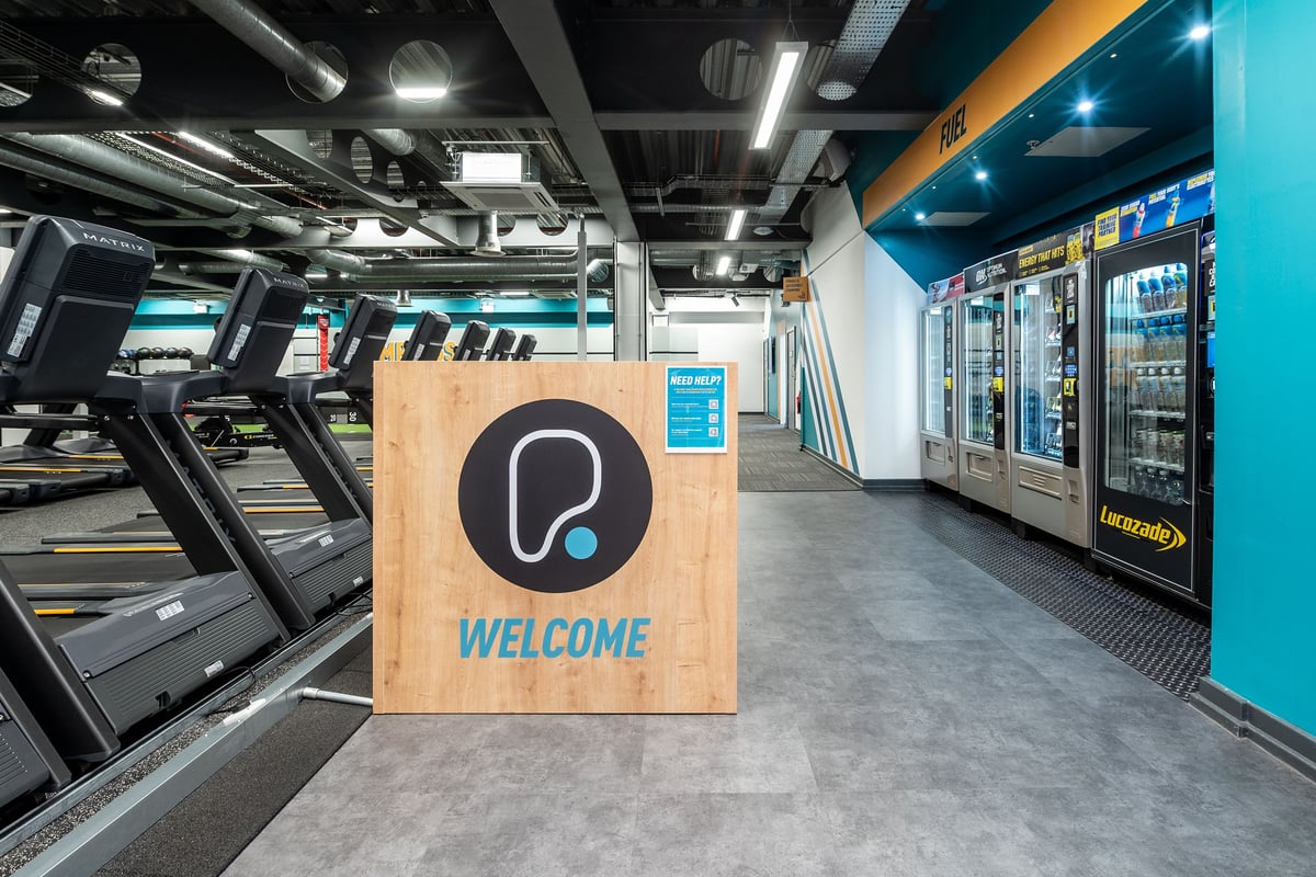 PureGym Manchester Spinningfields: Modern gym interior with treadmills, welcome sign, and blue accent walls.