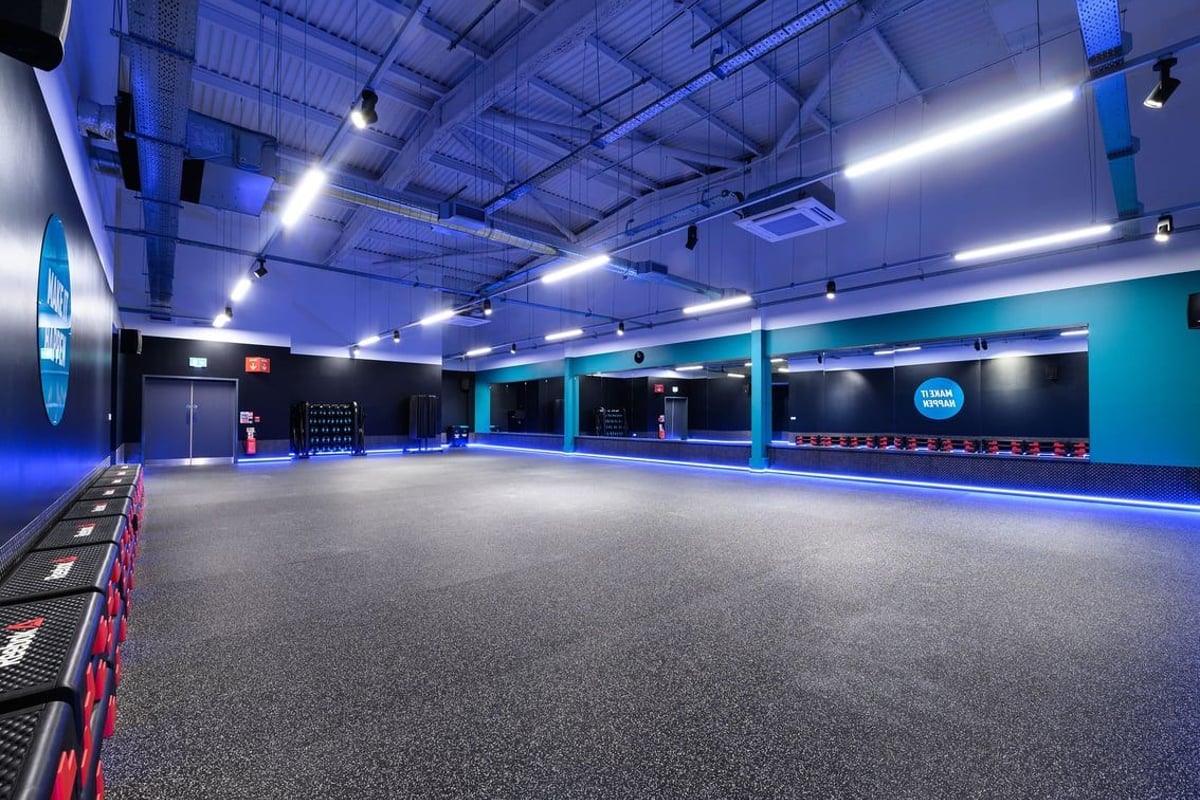 PureGym Romford: Large open fitness studio with mirrored walls, padded floor, neon lighting.