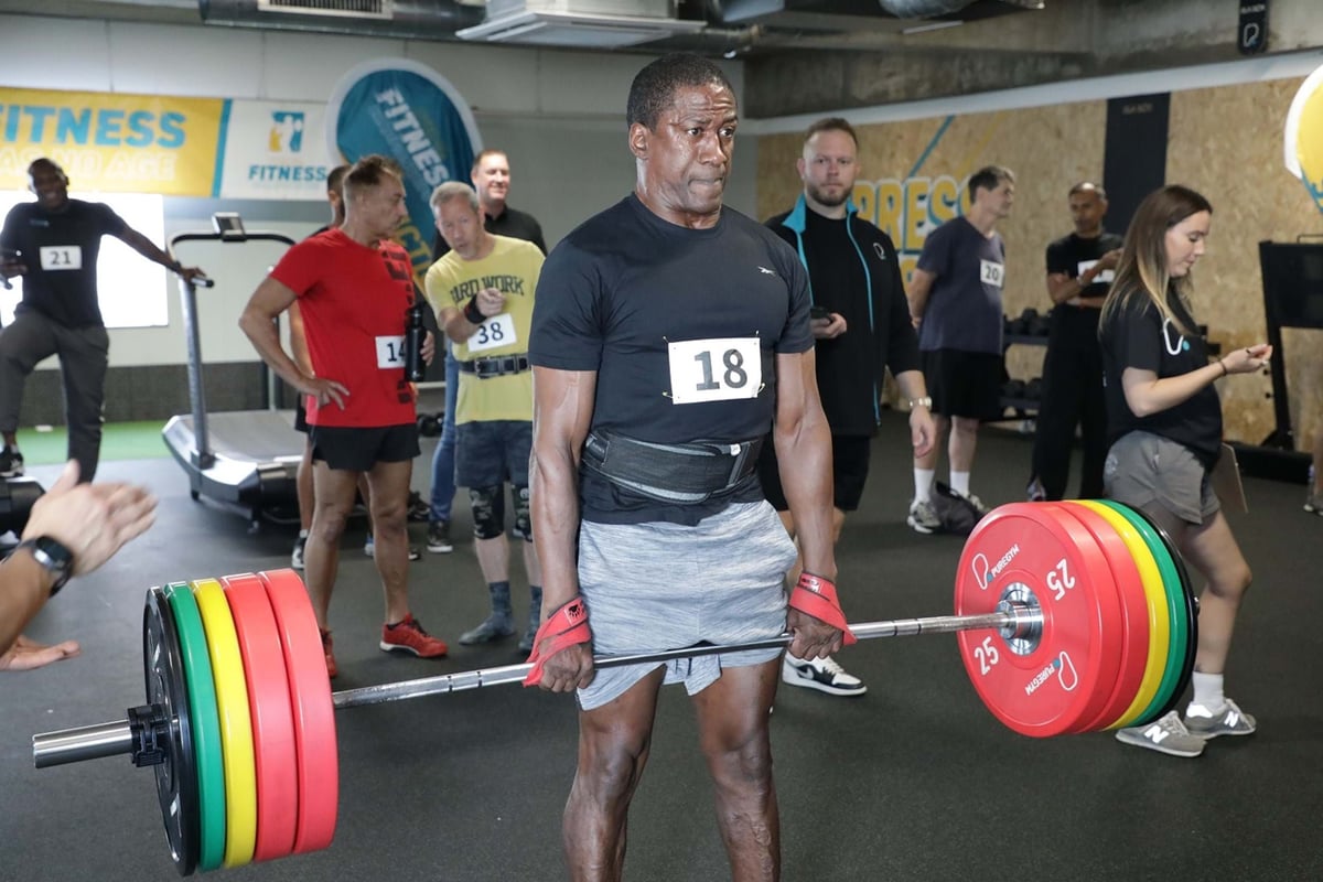 Man lifting heavy barbell in gym with people watching in background