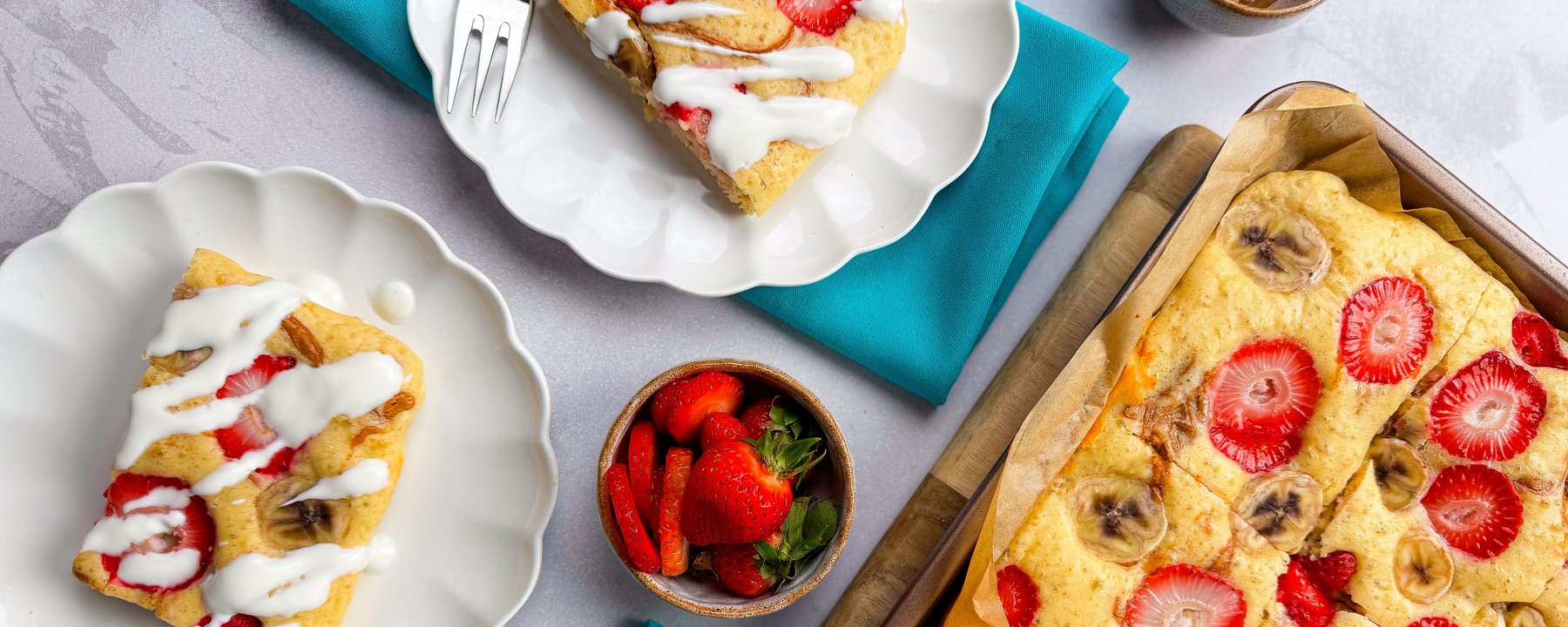 Sliced banana and strawberry traybake served on plates with white icing drizzle