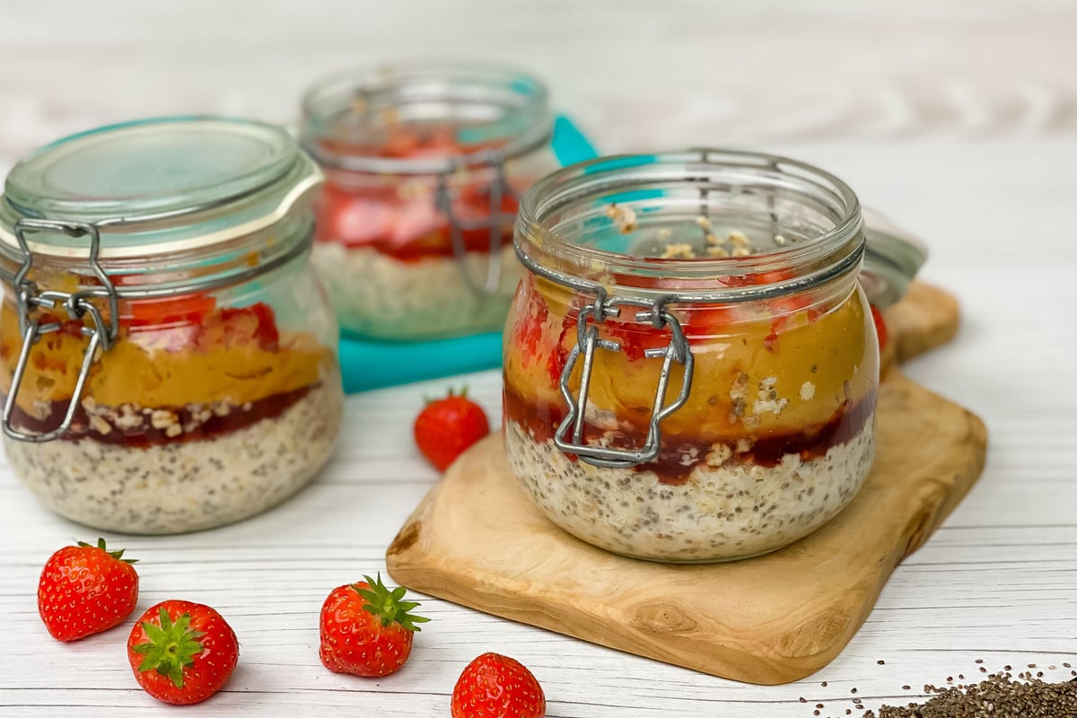 Layered overnight oats with chia seeds, jam and fruit in glass jars on wooden board