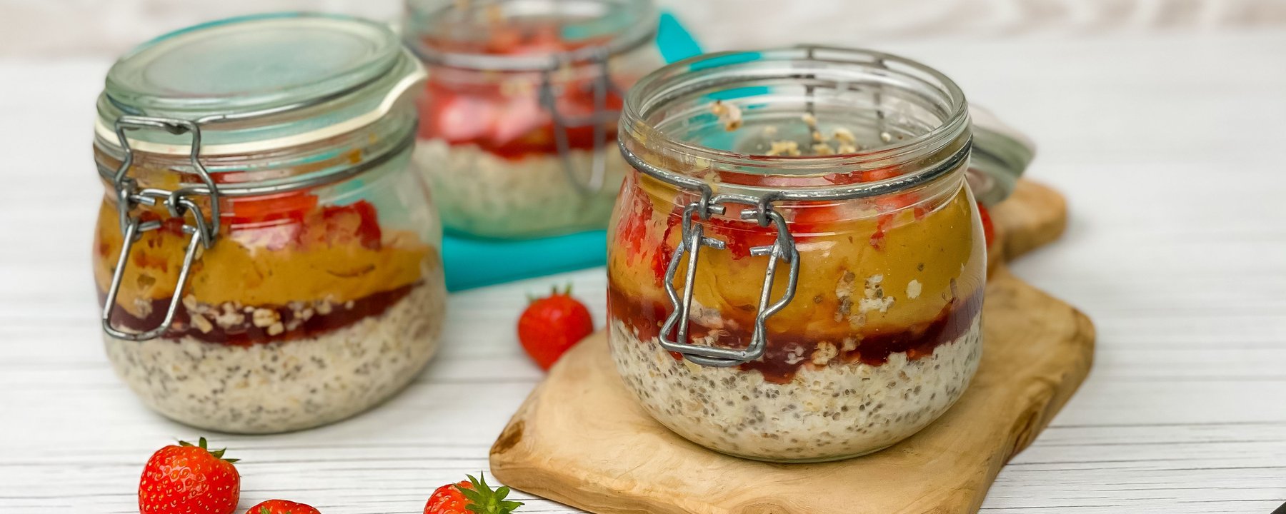 Layered overnight oats with chia seeds, jam and fruit in glass jars on wooden board