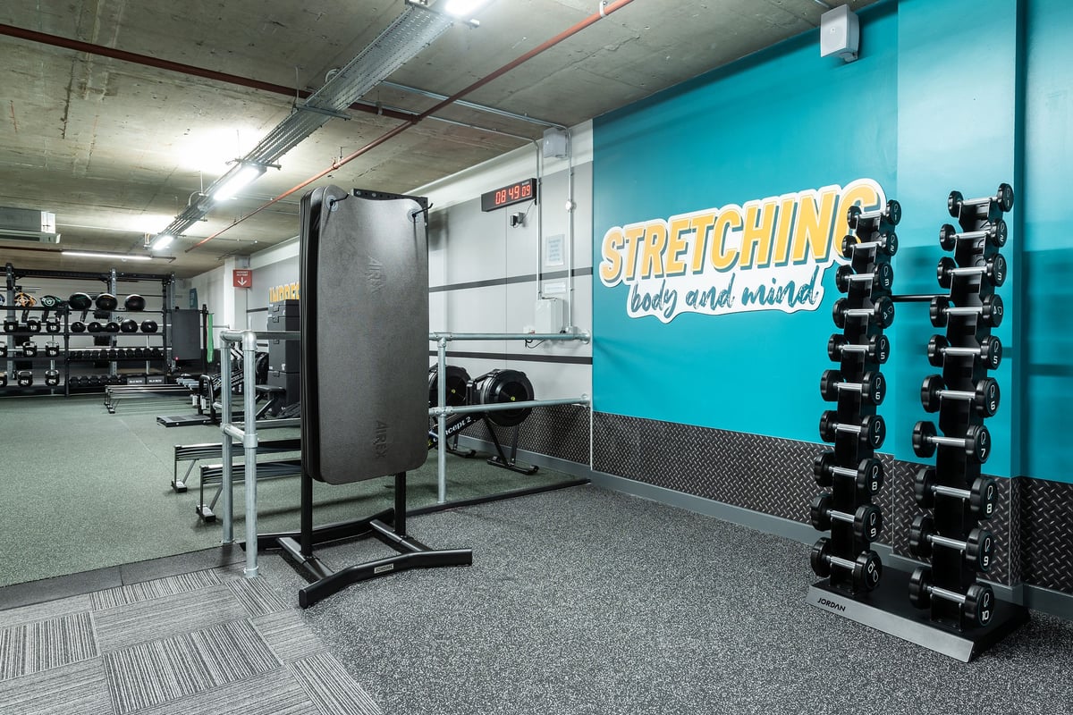 PureGym London Angel: Stretching area with padded benches, resistance bands, wall mirrors, and rubberized flooring.