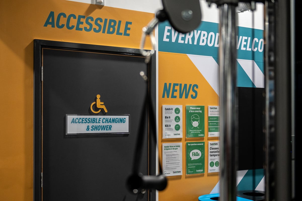 PureGym Swindon Stratton: Accessible changing and shower cubicle door, with "Everybodi Welco" and "News" signage visible.