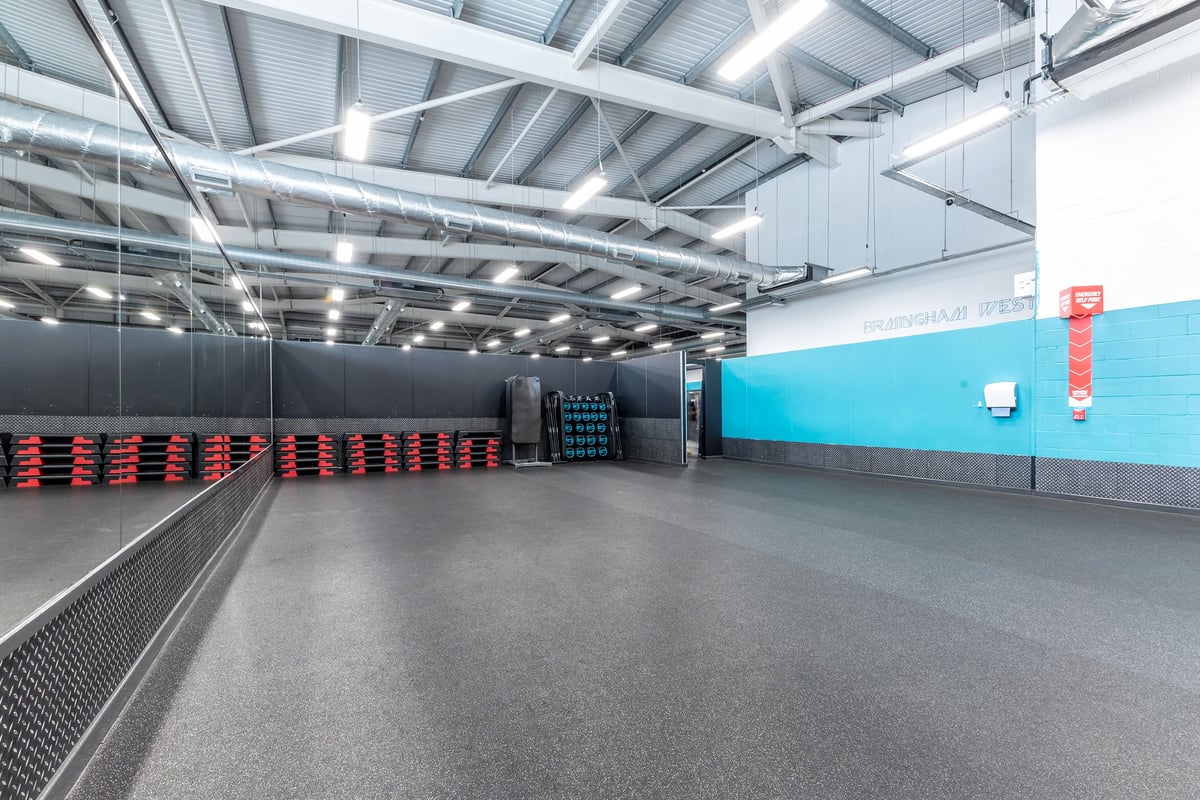 PureGym Birmingham West: Rows of weight plate trees, rubberized flooring, mirrored walls in a brightly lit gym interior.