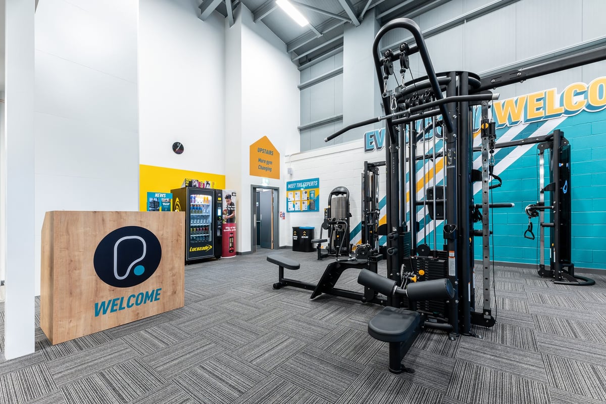PureGym Heanor: Resistance training machines, wooden logo panel, vending machines, benches, rubberized flooring.