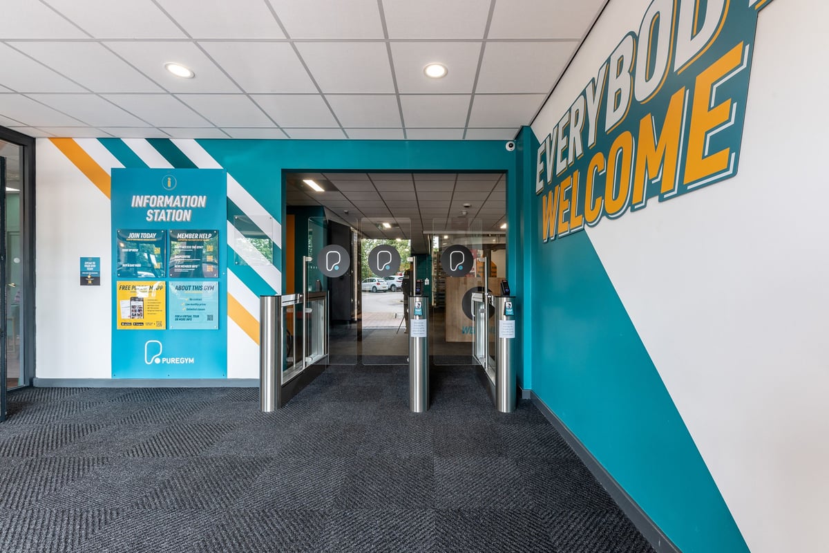 PureGym Sheffield Crystal Peaks: Entrance area with teal welcome signage, information station, and turnstiles.