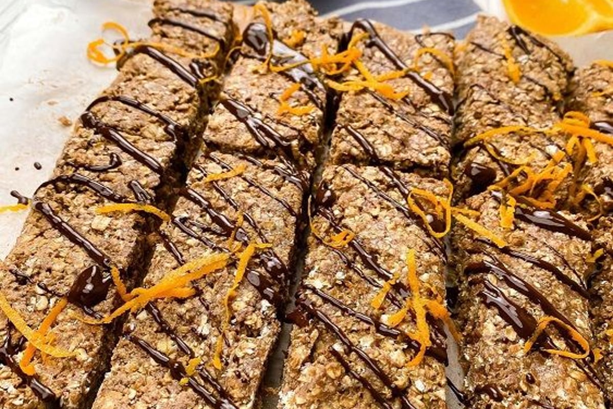 Oat bars drizzled with chocolate and orange zest on parchment with orange slices and sauce