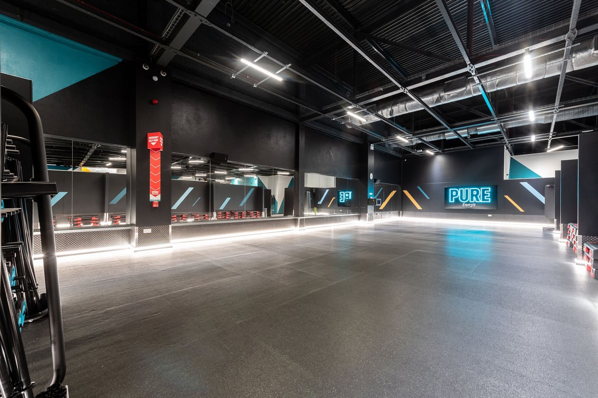 PureGym Southampton Bitterne: Gym studio with weights racks, Pure branding, rubberized floor, and neon blue-teal lighting.