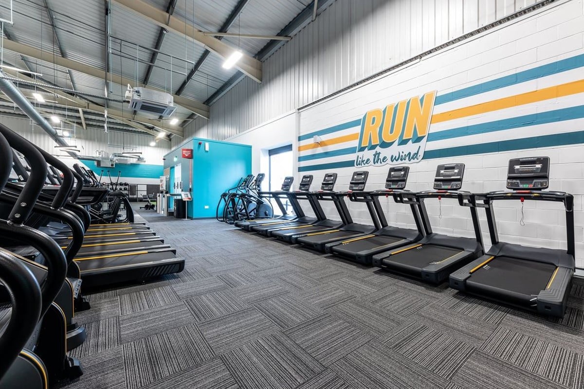 PureGym Merthyr Tydfil: Rows of treadmills alongside free weights and rubberised flooring in a fitness centre.