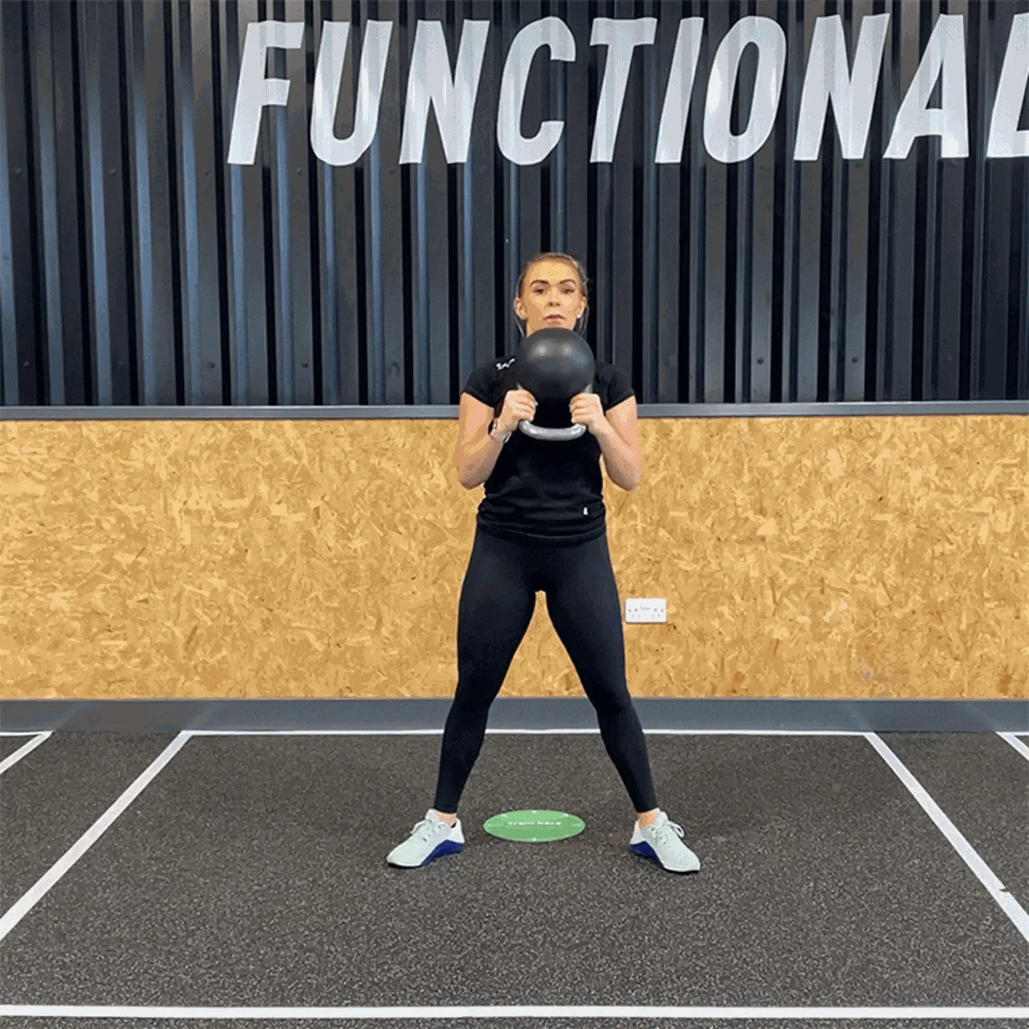 Woman in black sportswear lifting a kettlebell in a gym with FUNCTIONAL sign behind