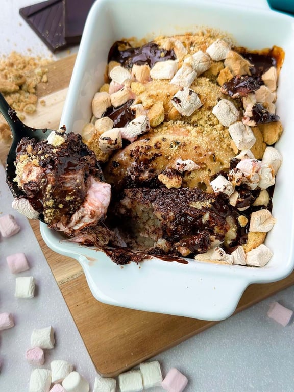 Baked s’mores dessert with melted chocolate, marshmallows, and biscuit crumbs in a white d