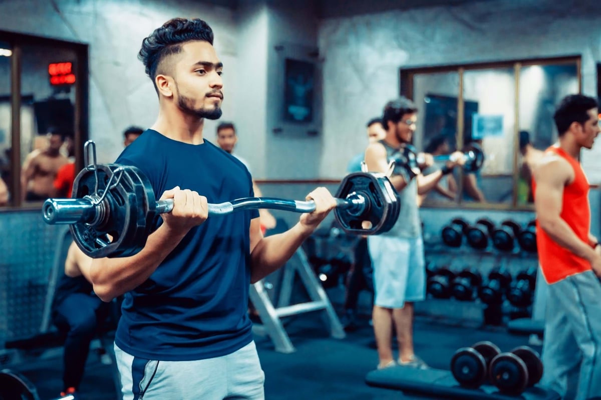 Young men lifting weights in a gym with mirrors and dumbbells in the background