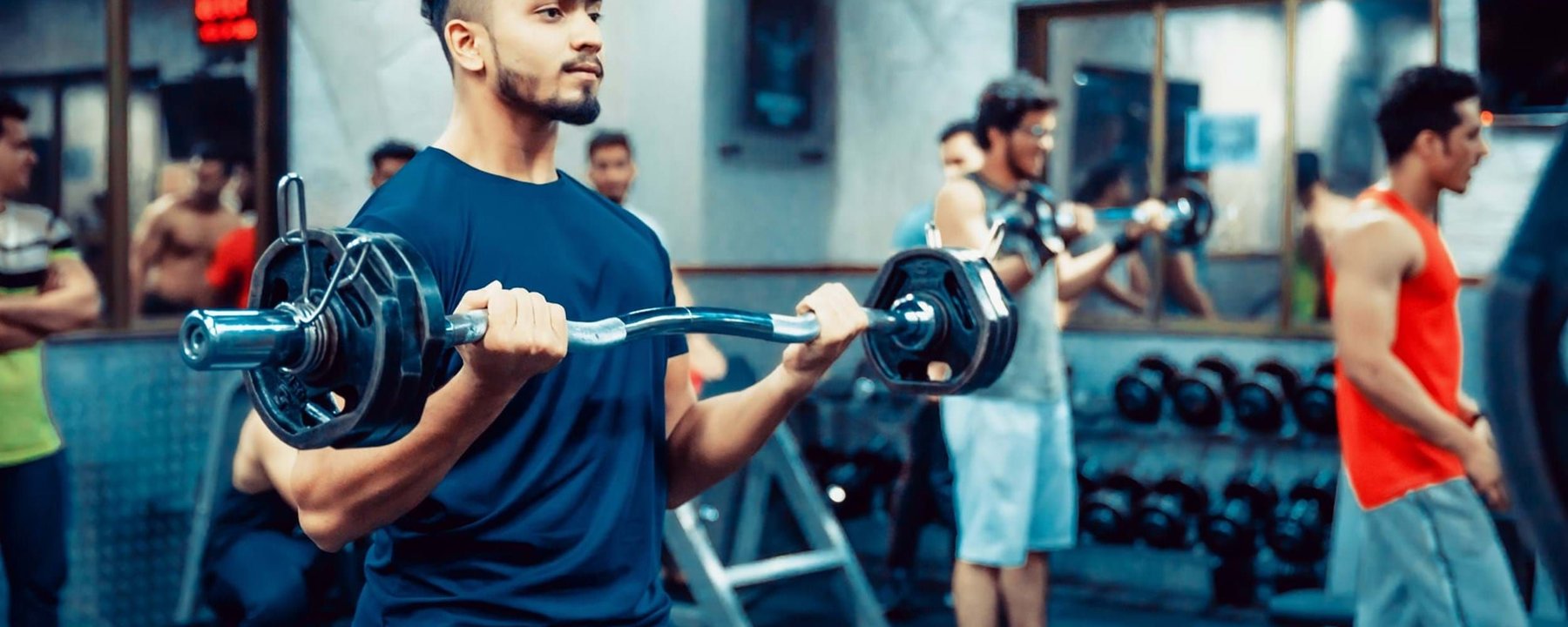 Young men lifting weights in a gym with mirrors and dumbbells in the background