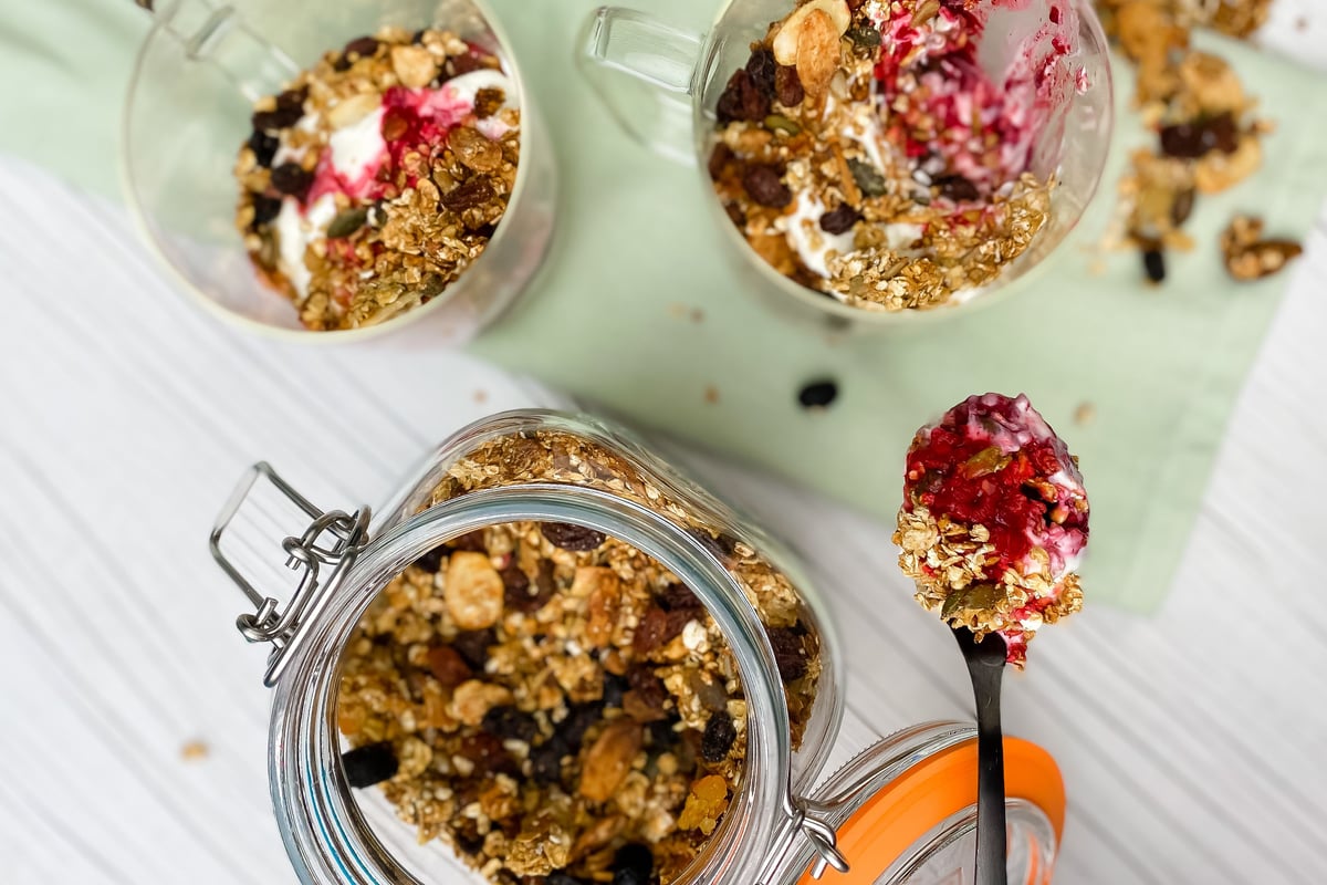Granola and yoghurt parfaits in glass jars with berry compote and spoon on table
