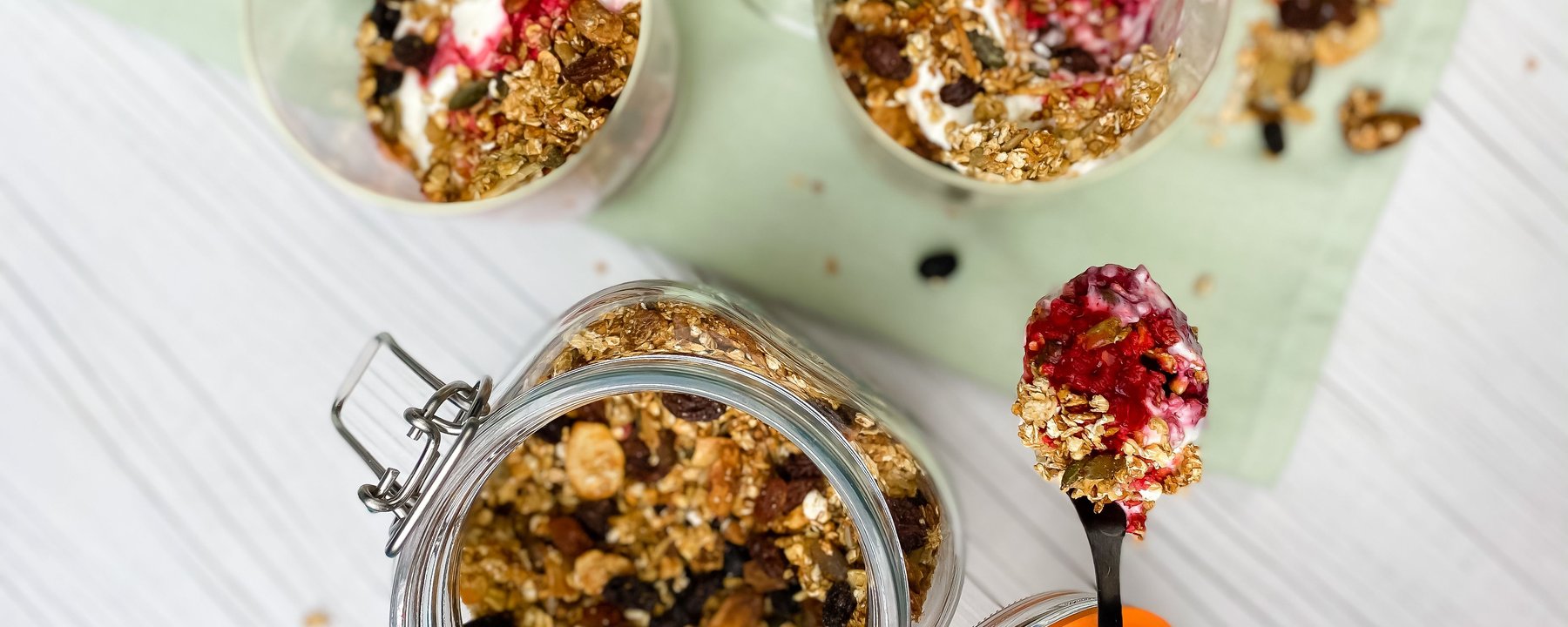 Granola and yoghurt parfaits in glass jars with berry compote and spoon on table