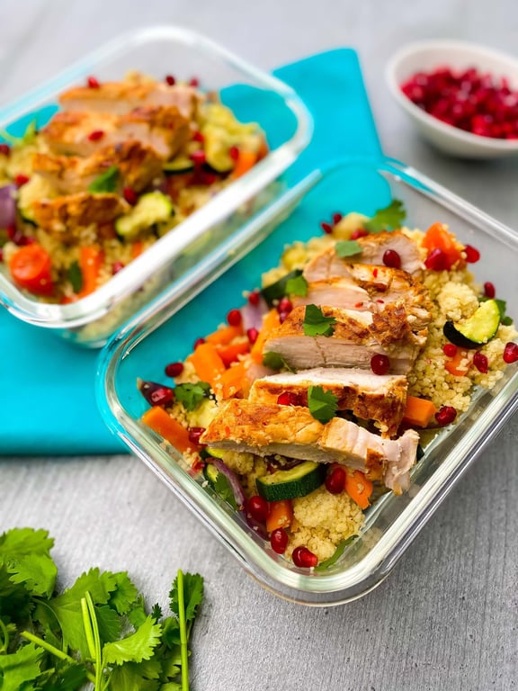 Grilled chicken slices on couscous with vegetables and pomegranate seeds in glass container