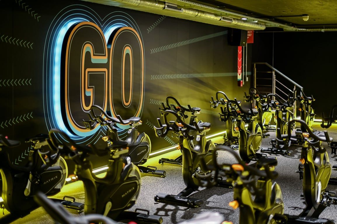 PureGym London Piccadilly: Rows of stationary bikes, neon "GO" signage, industrial lighting and design aesthetic.