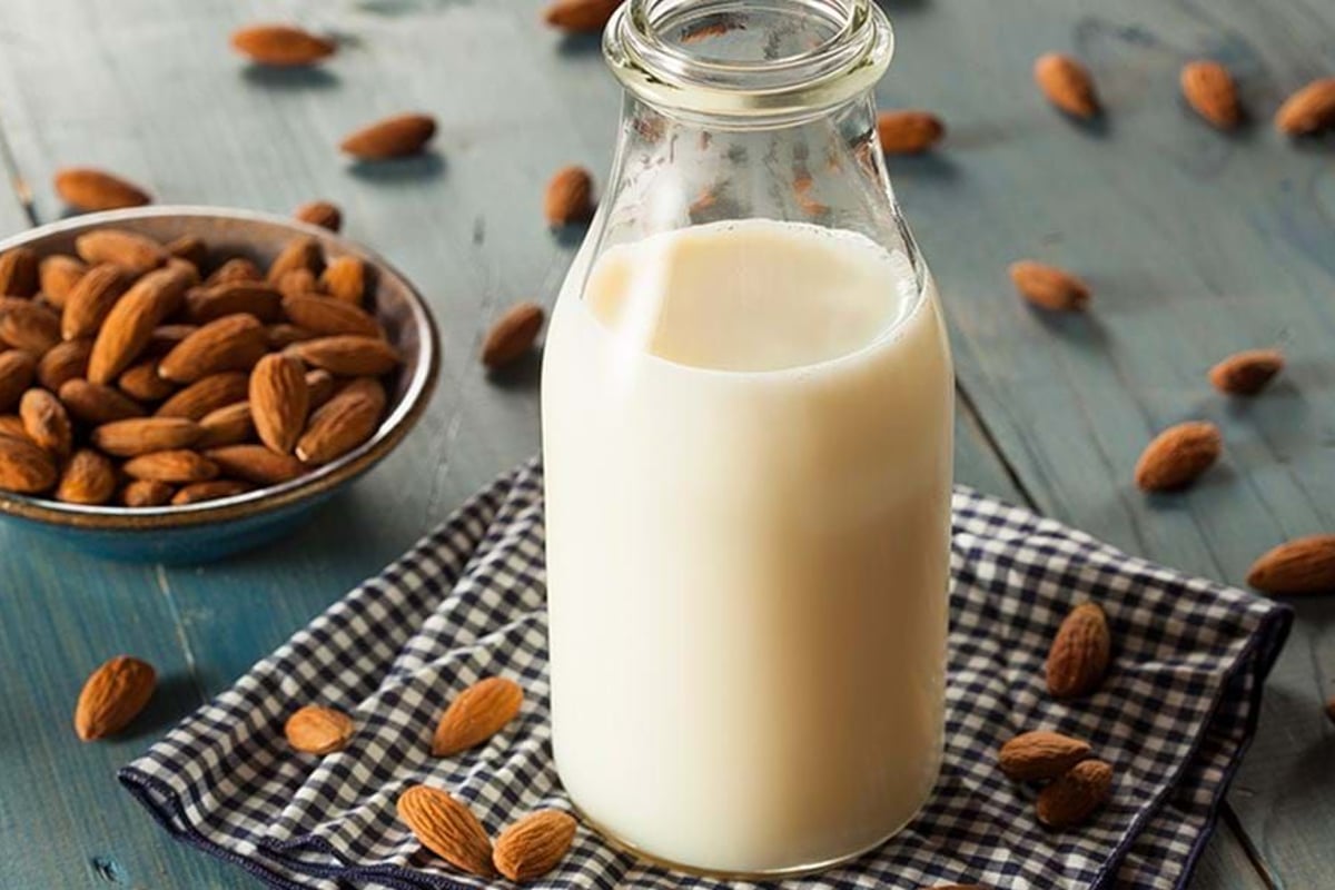 Glass bottle of almond milk on a checkered cloth with almonds scattered around