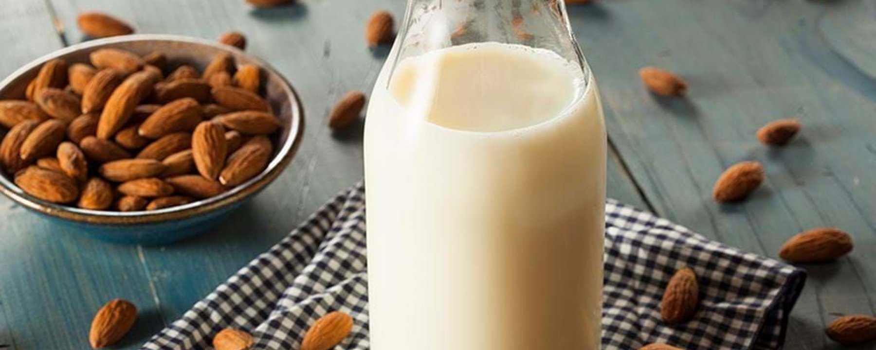 Glass bottle of almond milk on a checkered cloth with almonds scattered around