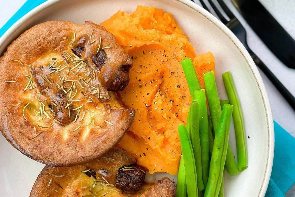 Two Yorkshire puddings with mashed sweet potatoes and green beans on a plate