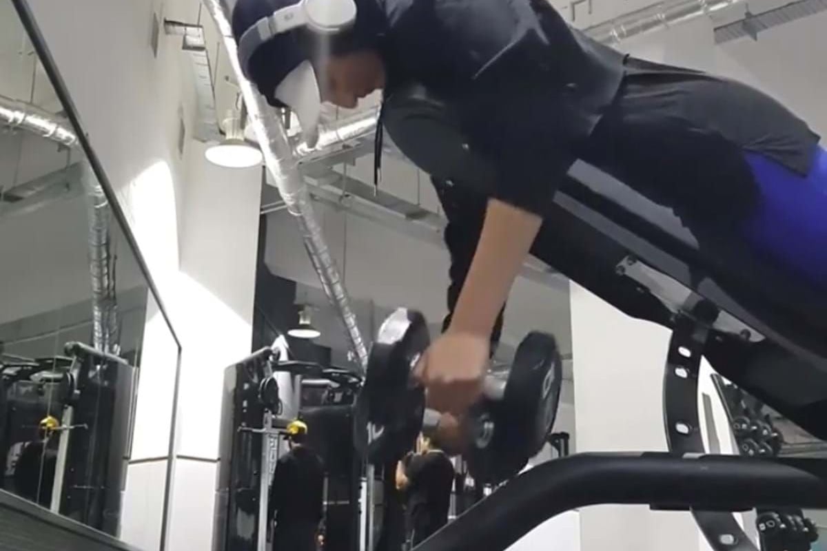 Person wearing headphones and a mask lifting dumbbells on an incline bench in gym