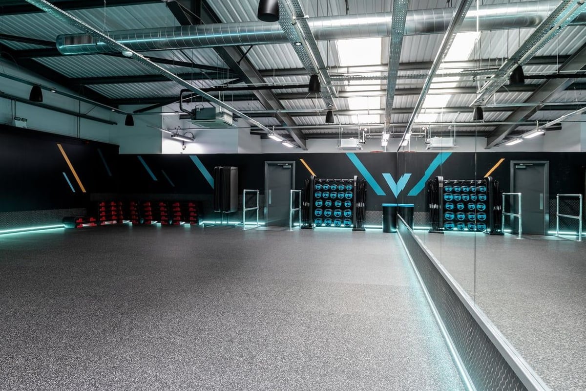 PureGym Oldham: Rubberized flooring, neon lighting, weight racks, and mirrored walls in a modern gym studio.