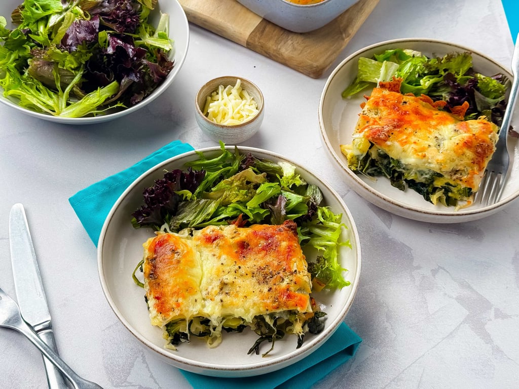 Two plates with spinach lasagne and mixed green salad on a white tablecloth