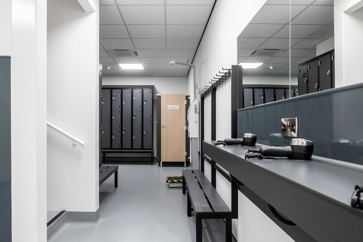 PureGym Taunton: Changing room lockers, benches, and mirrors lining the walls.
