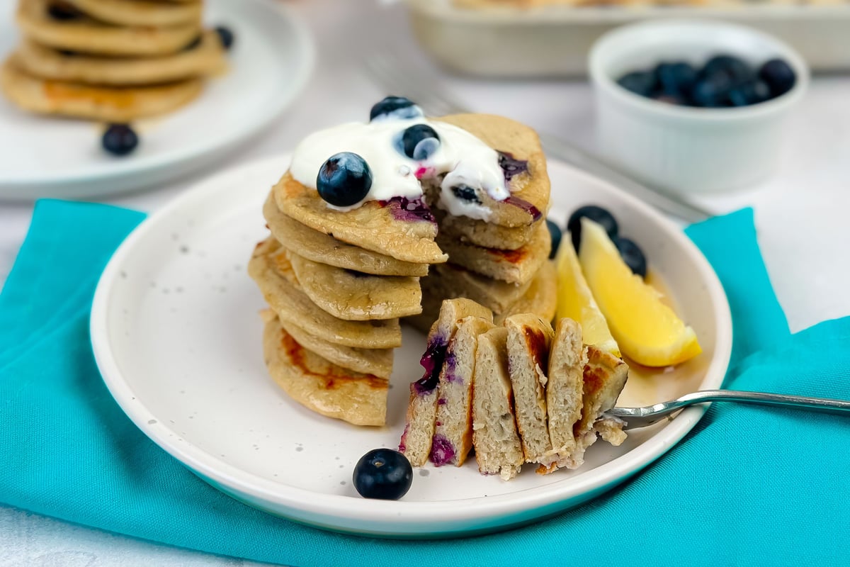 Stack of pancakes topped with blueberries and cream, sliced to reveal fluffy interior