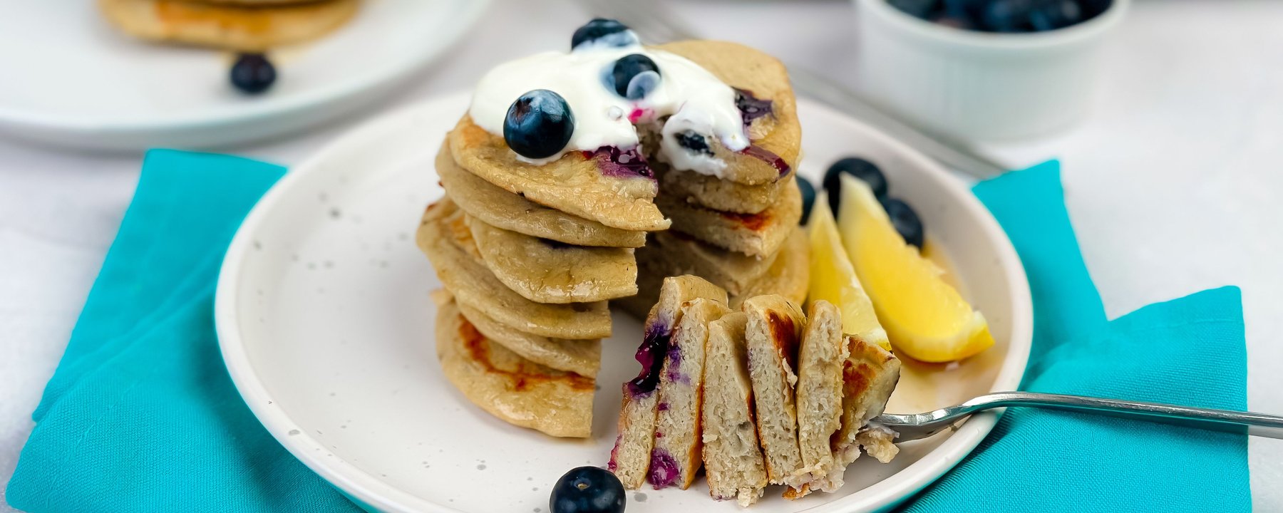 Stack of pancakes topped with blueberries and cream, sliced to reveal fluffy interior