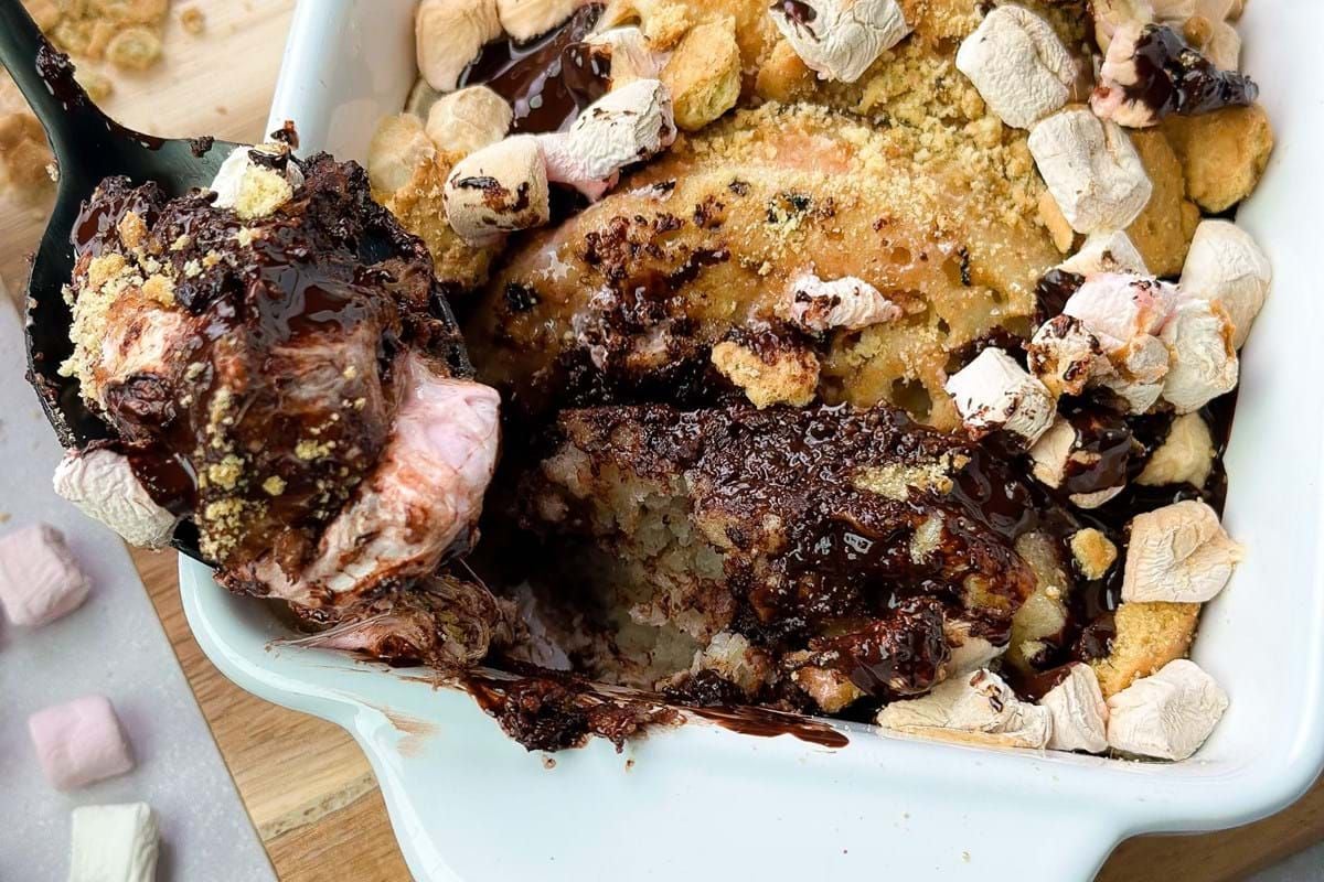 Baked s’mores dessert with melted chocolate, marshmallows, and biscuit crumbs in a white d