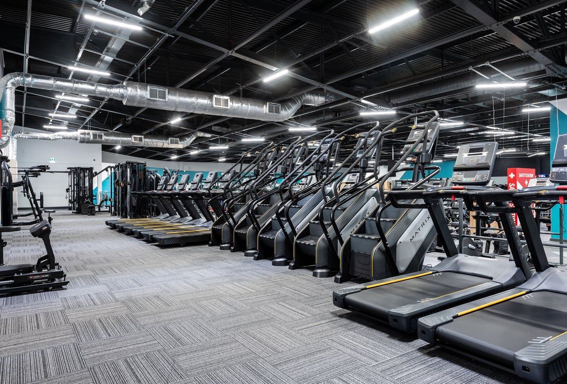 PureGym Southampton Bitterne: Rows of treadmills illuminated by bright lights and exposed ceiling infrastructure.