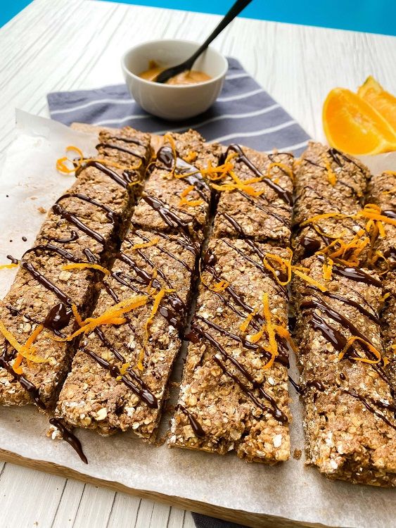 Oat bars drizzled with chocolate and orange zest on parchment with orange slices and sauce