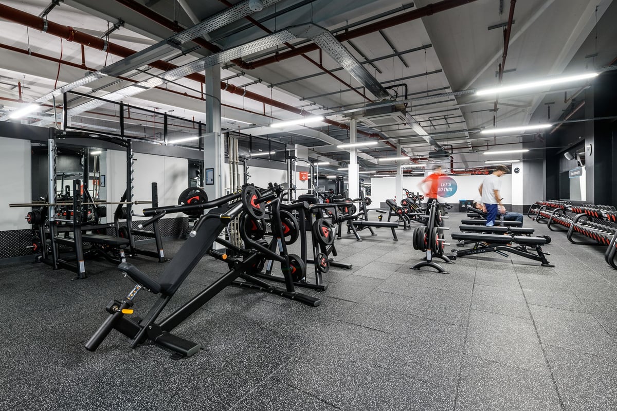 PureGym Cambridge Grafton Centre: Weight racks, benches, free weights, and rubberized flooring inside a dimly lit gym space.