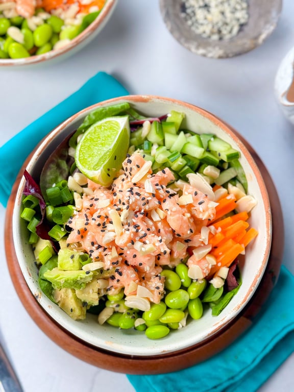 Bowl of poke with diced salmon, avocado, edamame, cucumber, carrot, lime, and sesame seeds