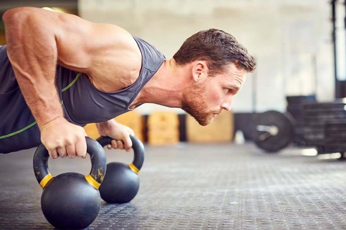 Man doing push-up using kettlebells in a gym with weights in the background