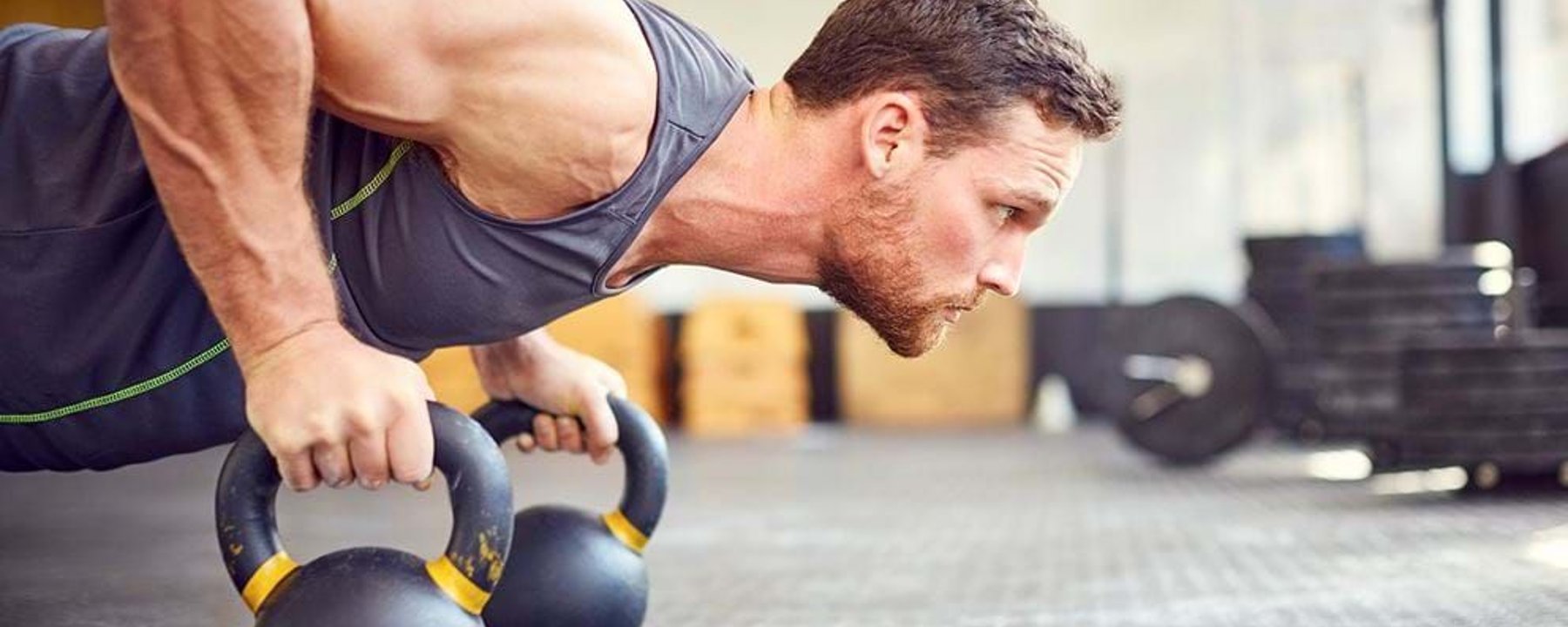 Man doing push-up using kettlebells in a gym with weights in the background
