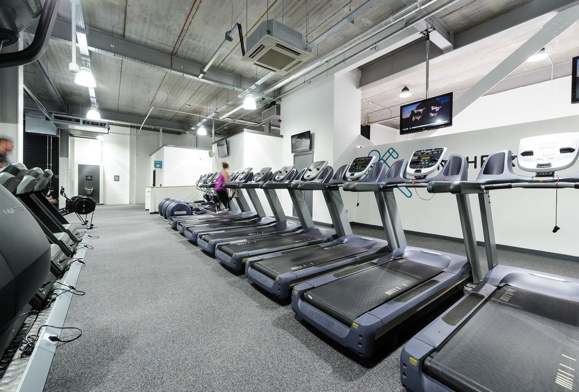 PureGym Bury: Rows of treadmills in an industrial-style gym with exposed ceilings and TV screens.