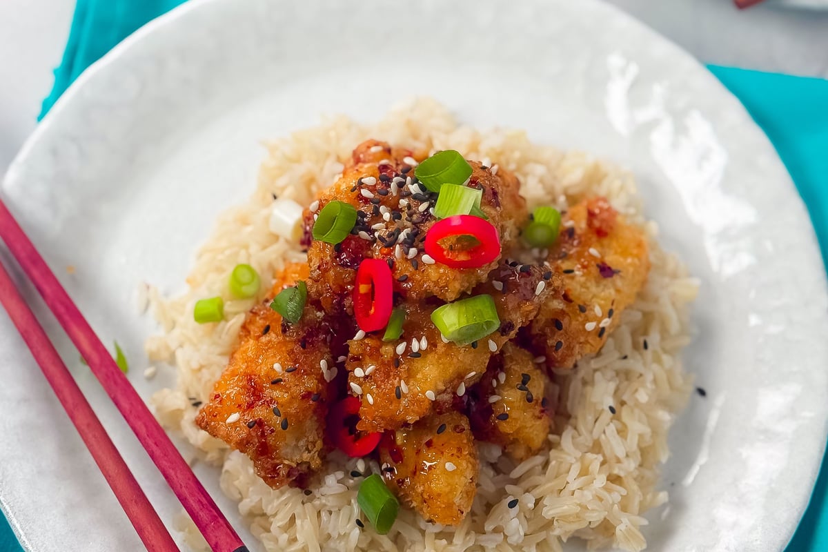 Crispy chicken pieces on white rice with red chilli slices, spring onion and sesame seeds