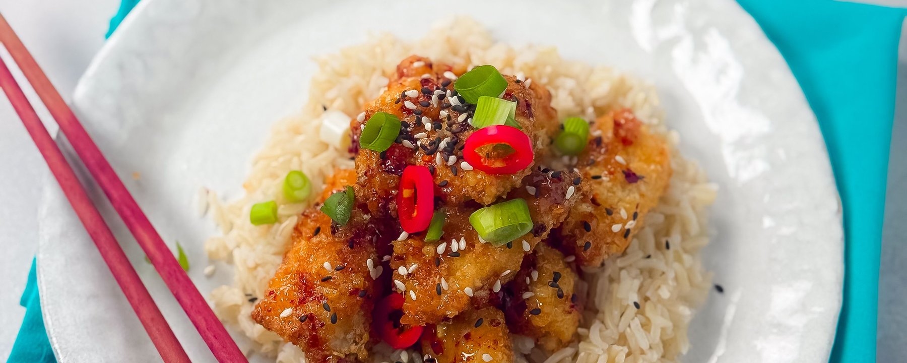 Crispy chicken pieces on white rice with red chilli slices, spring onion and sesame seeds