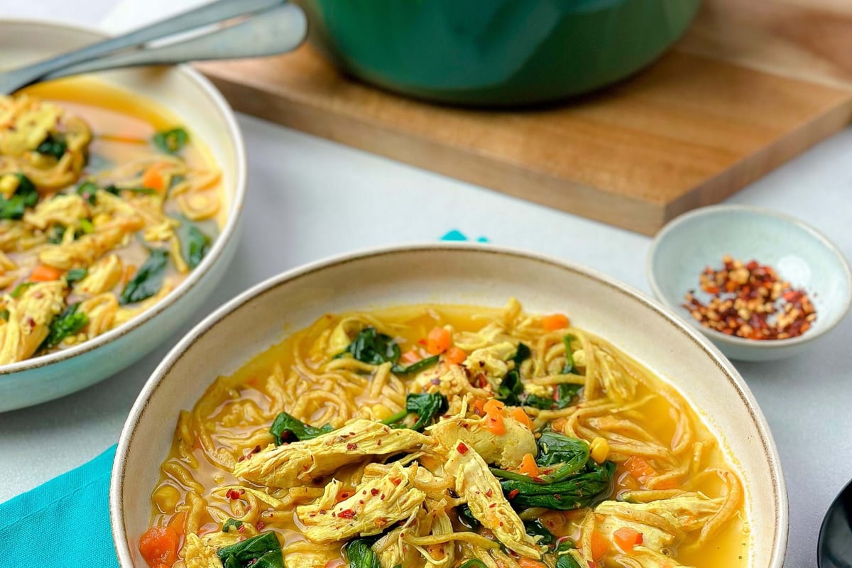 Bowls of chicken noodle soup with spinach and diced carrots on a tablecloth.
