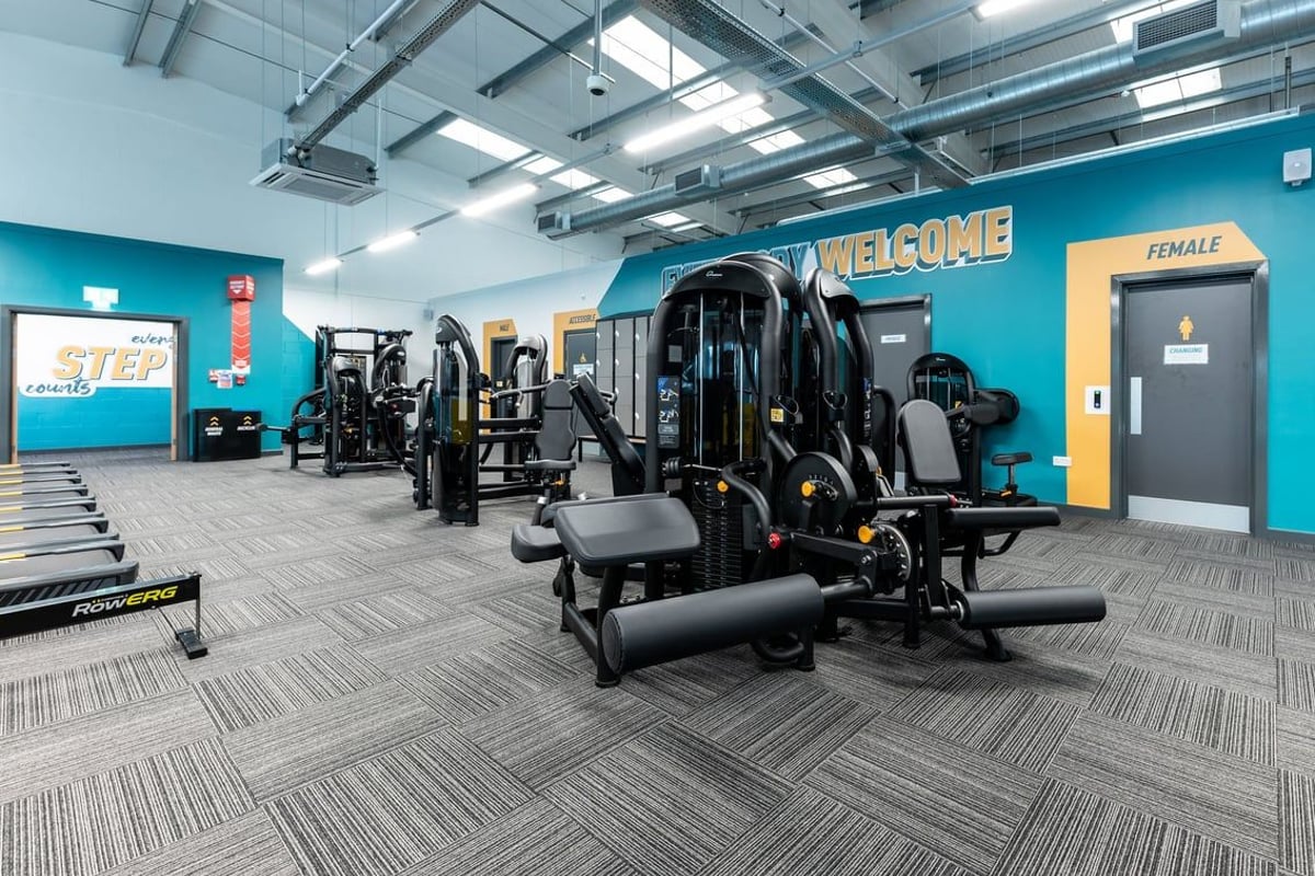PureGym Caerphilly: Resistance machines, benches, free weights on rubberized gym flooring near a female restroom sign.