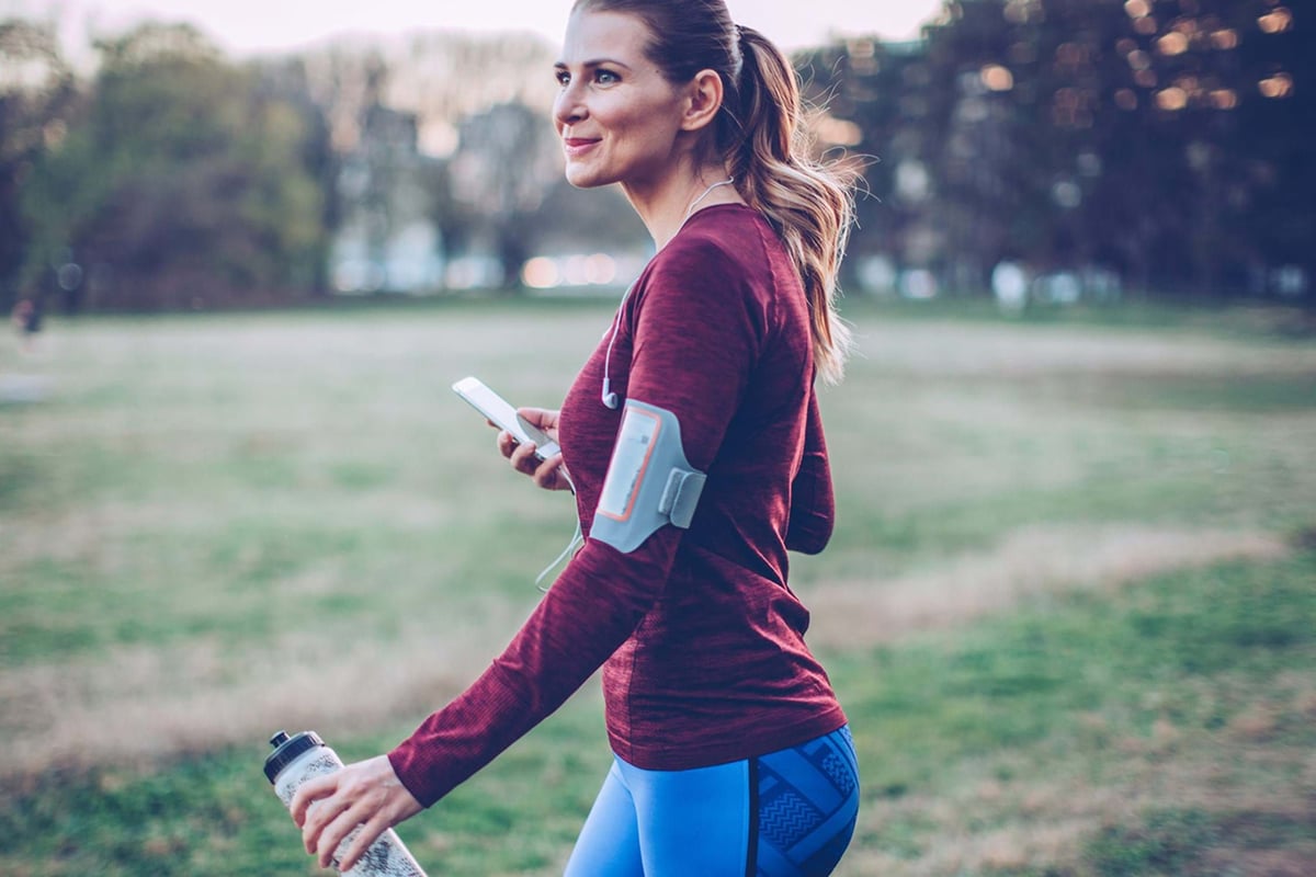 Woman in sportswear holding a water bottle and phone in a park at dusk