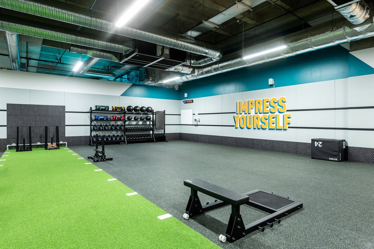 PureGym Uxbridge: Weight racks, turf area, benches, freeweights, mirrored wall with motivational signage.